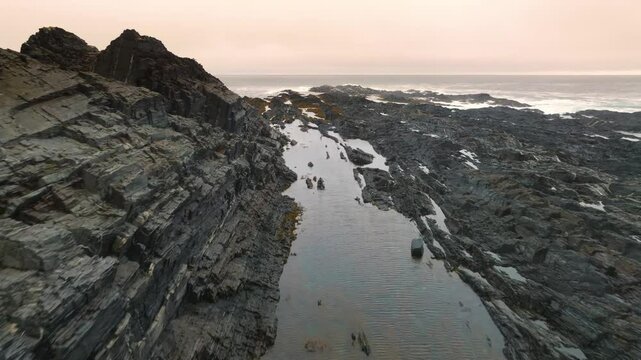 This footage features a rugged coastline with igneous and metamorphic rocks, illustrating geological processes of magma solidification and rock alteration under heat and pressure.