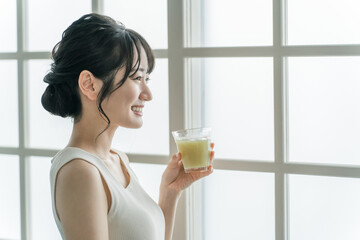 家でグリーンスムージーを飲む笑顔のアジア人女性
