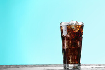 Refreshing cola with ice cubes in glass on dark textured table against turquoise gradient background, closeup. Space for text
