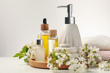 Spa products, pebble stones and twigs with beautiful flowers on white table, closeup