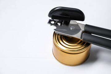 Obraz premium Can opener and tin on white wooden table, closeup. Space for text