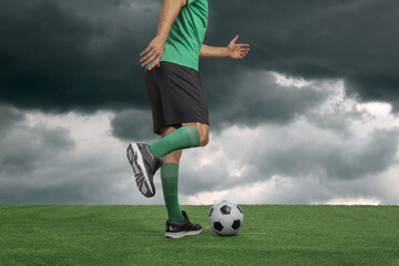 Football player kicking soccer ball under gloomy sky, closeup
