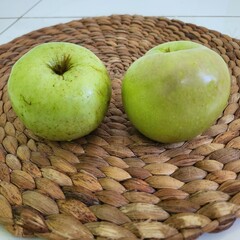 Two fresh green apples on a woven placemat.