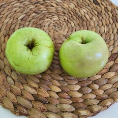 Two vibrant green apples resting on a woven placemat.