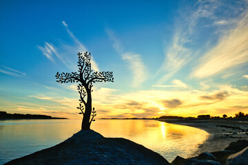 Tree Cross on a rock with a sunset bay of water in the background.