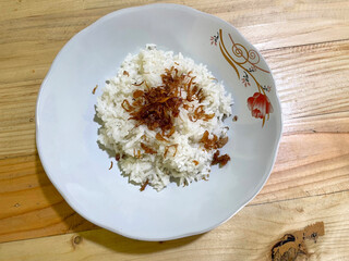 White rice with fried onions on top on a white plate with floral motifs on a wooden table. rice as food