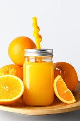 Mason jar of fresh orange juice and plate with fruits on white background