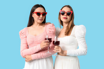 Beautiful young lesbian couple with glasses of wine on blue background
