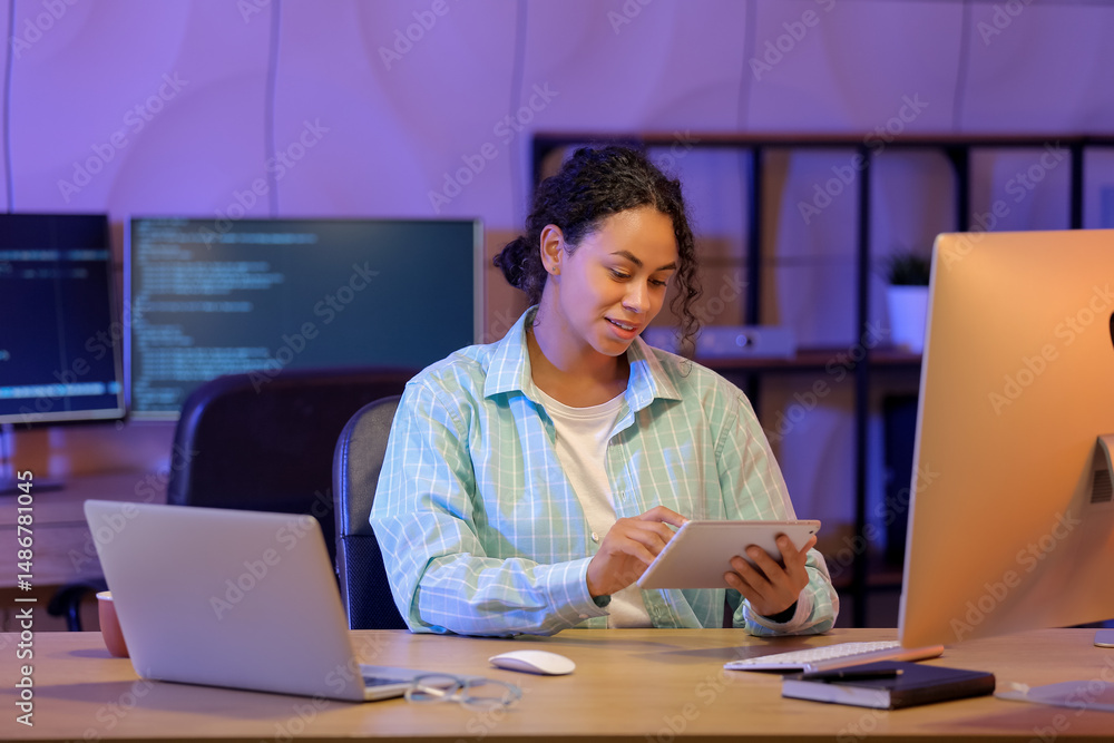 Aufkleber young african-american qa engineer working with tablet computer in office at night