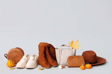 Different shoes with stylish bags, brown hat, pumpkins and autumn leaves on grey background