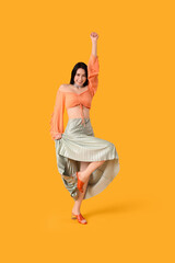 Happy young woman in skirt dancing on yellow background