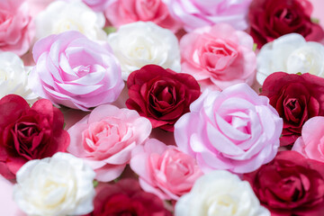 ピンクの背景に並べられた色とりどりの造花のバラ