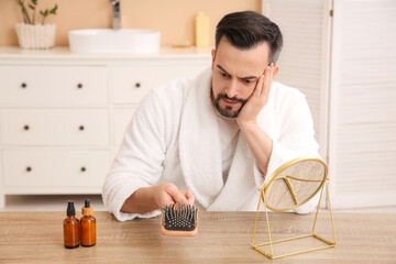 Worried young man with hair loss problem and brush in bathroom