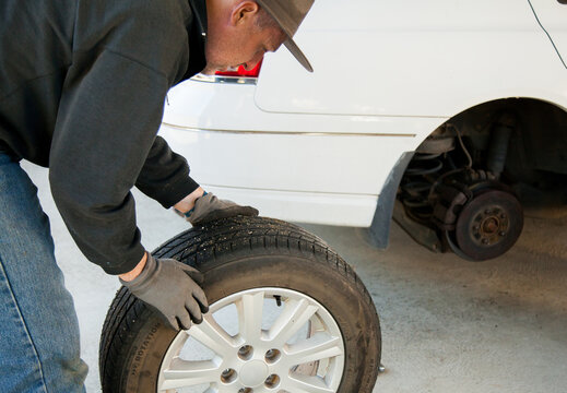 Man rolling flat tyre away from car to fix it