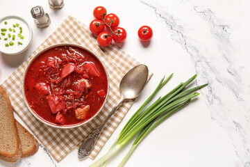 Bowl of tasty Ukrainian borscht with sour cream, green onion and bread slices on white background