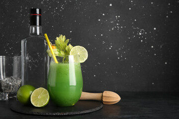 Glass of green bloody mary cocktail garnished with lime, physalis berry and cucumber slice on black...