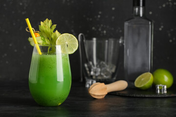 Glass of green bloody mary cocktail garnished with lime, physalis berry and cucumber slice on black...