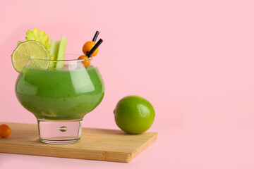 Glass of green bloody mary cocktail garnished with physalis berries and lime on pink background