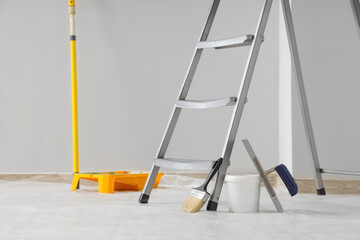 Metal stepladder with painter's tools near light wall in room