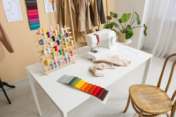 Tailor's workplace with sewing machine, thread spools and fabric samples in atelier