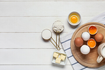 Cutting board with fresh chicken eggs, butter, flour and sugar on light wooden background