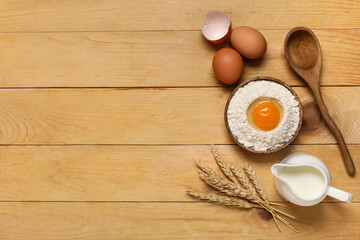 Composition with plate of flour, fresh chicken eggs, milk and spikelets on wooden background