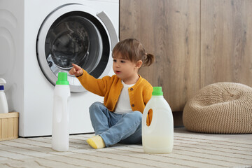 Cute little girl with laundry detergents on floor at home. Child in danger