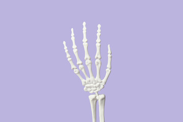 Raised hand of human skeleton on lilac background