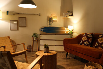 Interior of stylish living room with brown sofa, armchair, glowing lamps and surfboard at evening