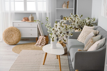 Interior of light living room with sofa and flowering branches