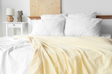 Cozy bed with soft pillows and yellow blanket in light bedroom