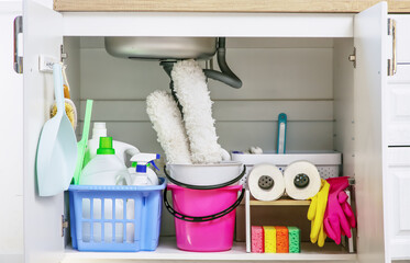 Baskets and bucket with different cleaning supplies and paper towels under sink in kitchen