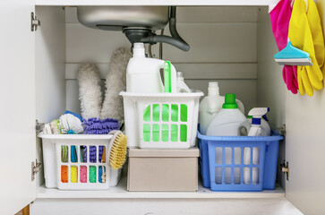 Baskets with different cleaning supplies under sink in kitchen