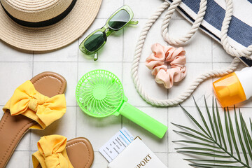 Bag with female summer accessories, passport, ticket and mini fan on light tile background