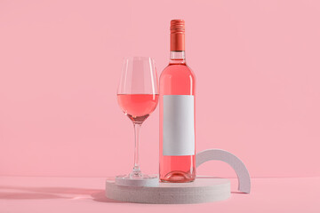 Bottle of wine with blank label and glass on stand against pink background