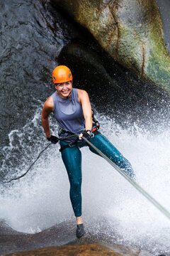 Adventurous female athlete rappelling down a waterfall, enjoying extreme sports in a canyoning adventure during summer