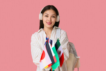 Young Asian woman with flags of different countries, headphones and backpack on pink background