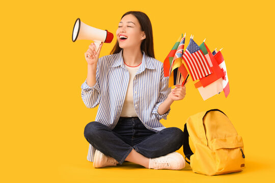 Female Asian student with flags of different countries and megaphone on yellow background