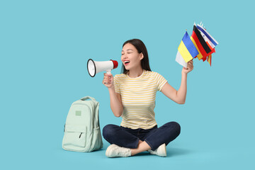 Female Asian student with flags of different countries and megaphone on blue background
