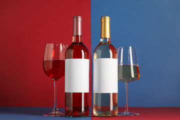 Bottles of different wine with blank labels and glasses on color background