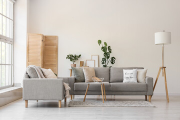 Interior of light living room with grey sofas, lamp and folding screen