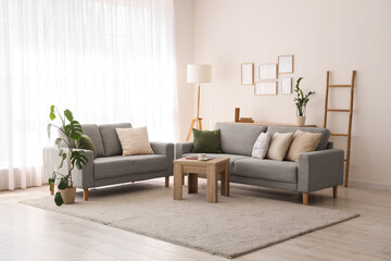 Interior of light living room with grey sofas, ladder and lamp