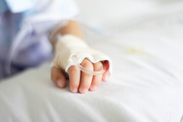 Child's hand with a Saline intravenous (iv) drip resting on a hospital bed, symbolizing medical care, recovery, and compassion in a clinical setting.