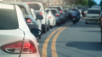 Rear side of white car with turn on brake light. Aura of red light from the rear of the car. Traffic congestion stretches along a curve. Parallel yellow traffic lines on the asphalt surface.