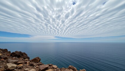 expansive view of the sea from a rocky viewpoint, with a sky completely filled with layered stratus clouds stretching evenly across the horizon