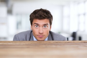 Man peeking over a wooden surface looking surprised in an office setting.