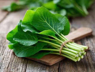 Fresh green leafy vegetable with large dark green leaves and thick stems, tied with string, placed on rustic wooden surface, evoking freshness and natural health benefits