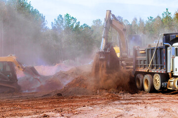 Heavy machinery works to excavate move dirt at construction site surrounded by trees on...