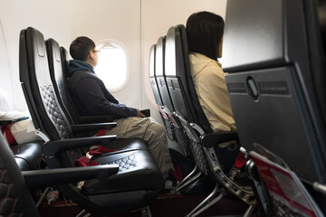 Interior view of commercial airplane with teenage man passenger sitting next to the window.Traveler young asian man sits in a plane and looking outside.