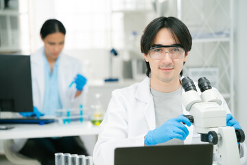 scientist and researcher in laboratory setting works with microscope while colleague conducts...
